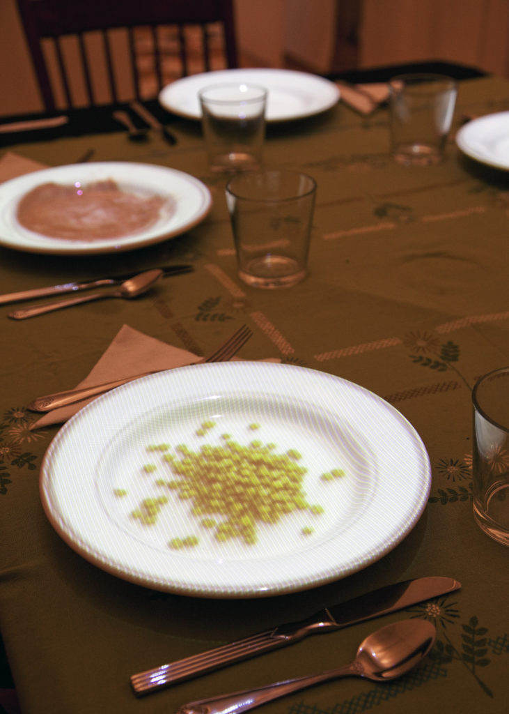 A video installation about hunger and chance - a photo of plates on a table showing projected video images, one of corn kernals