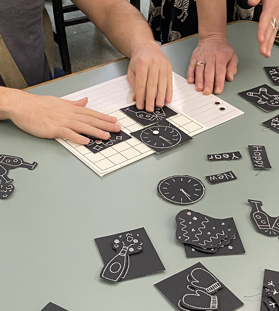 A workshop participant arranges three design elements (a clock, a party horn, and champagne glasses) on to a raised line grid. 