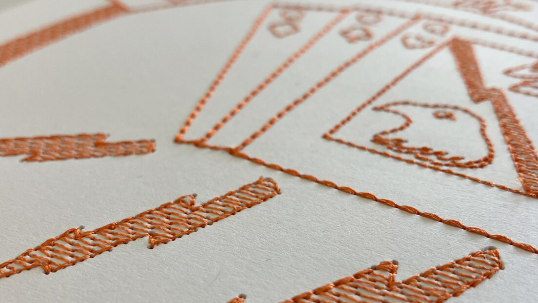 Orange on white embroidery featuring card shapes with eagles and lightning bolts representing Digital Embroidery for Tactile Graphics